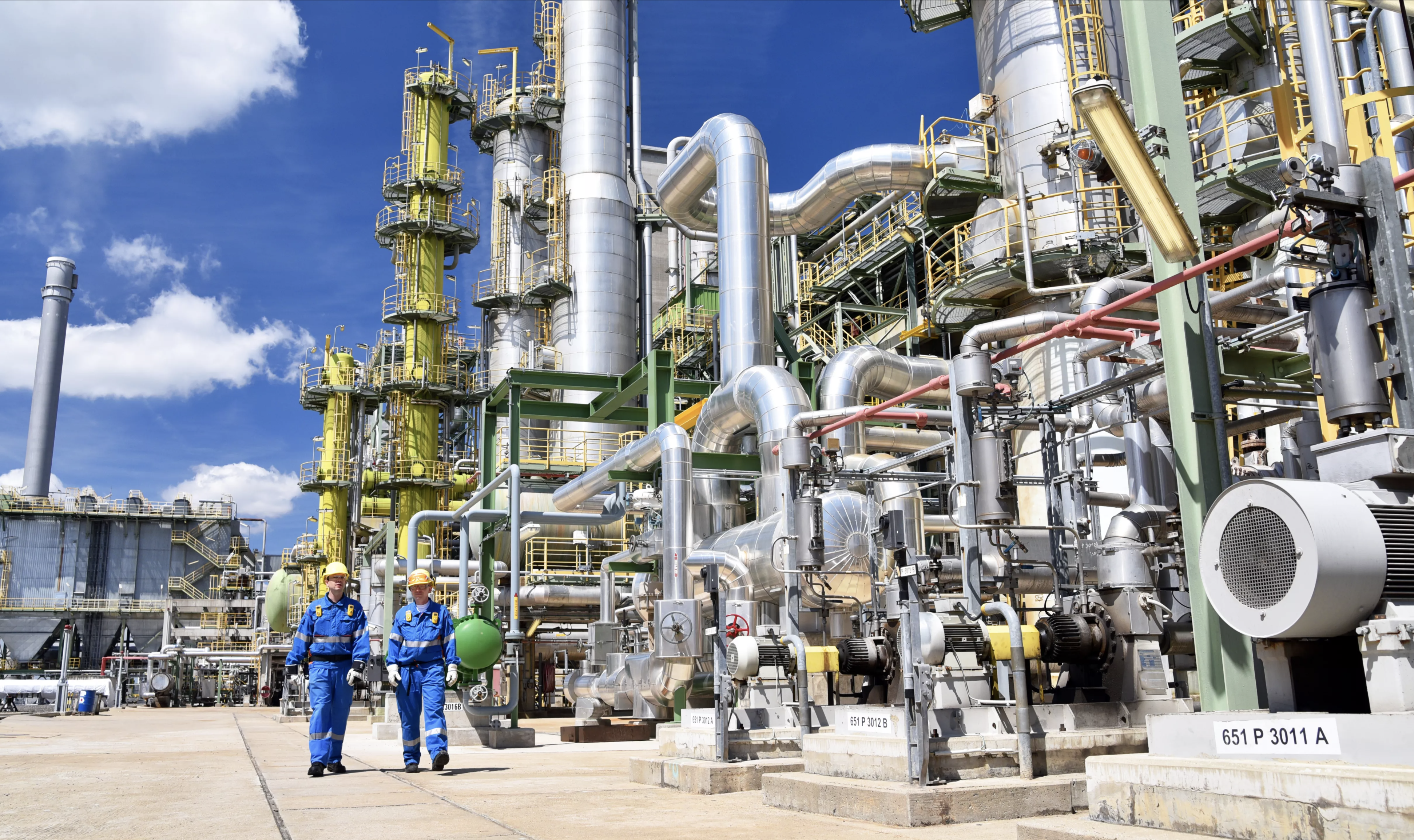 Chemical plant with workers walking past pipework