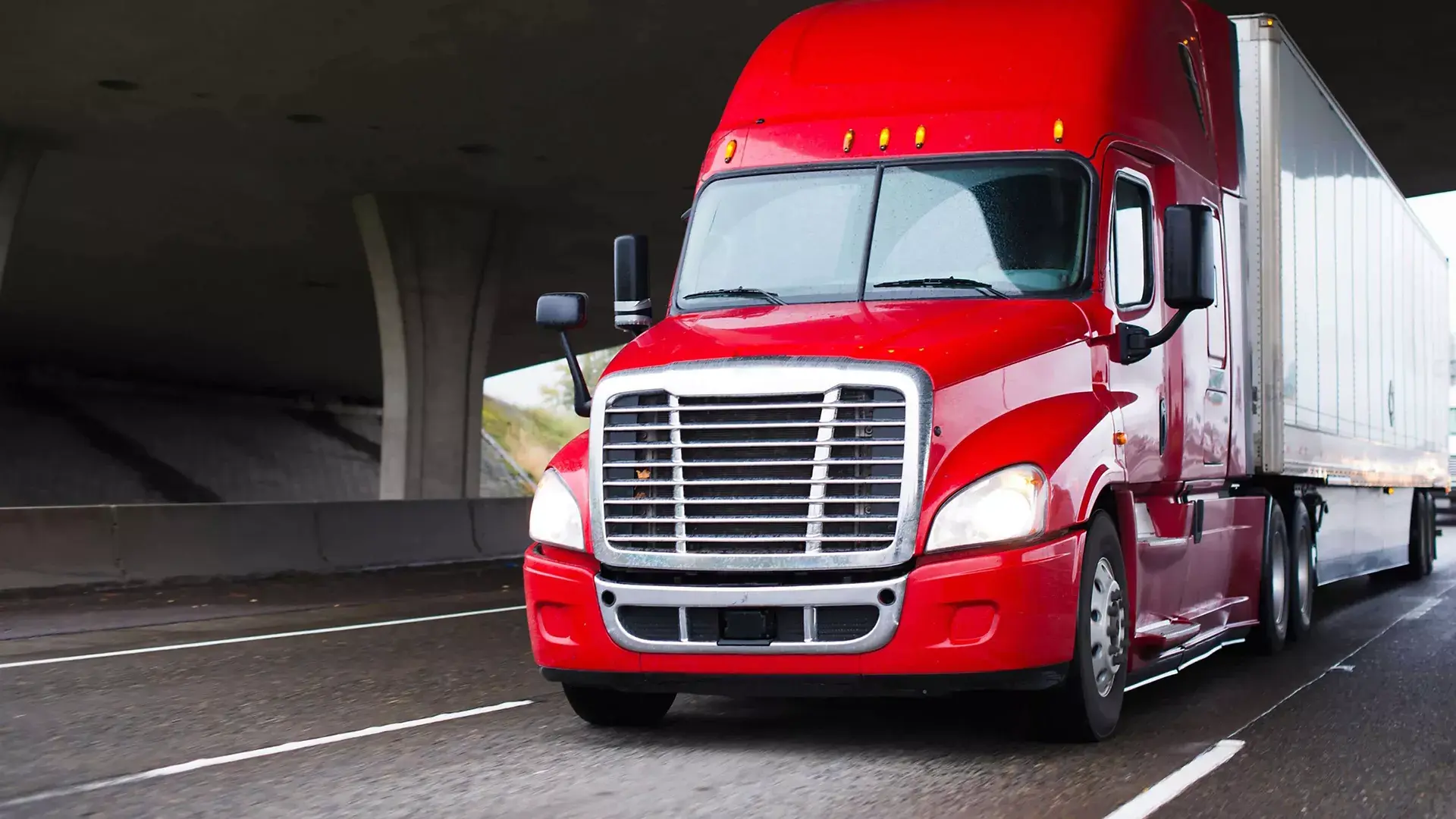 Red semi-truck and trailer under an overpass